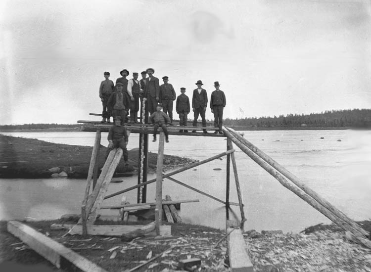 Svartvit bild, flera människor på träställning i vattenbryn.