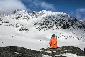 Person sitter på ett kalt berg i ett i övrigt snätäckt fjällandskap.