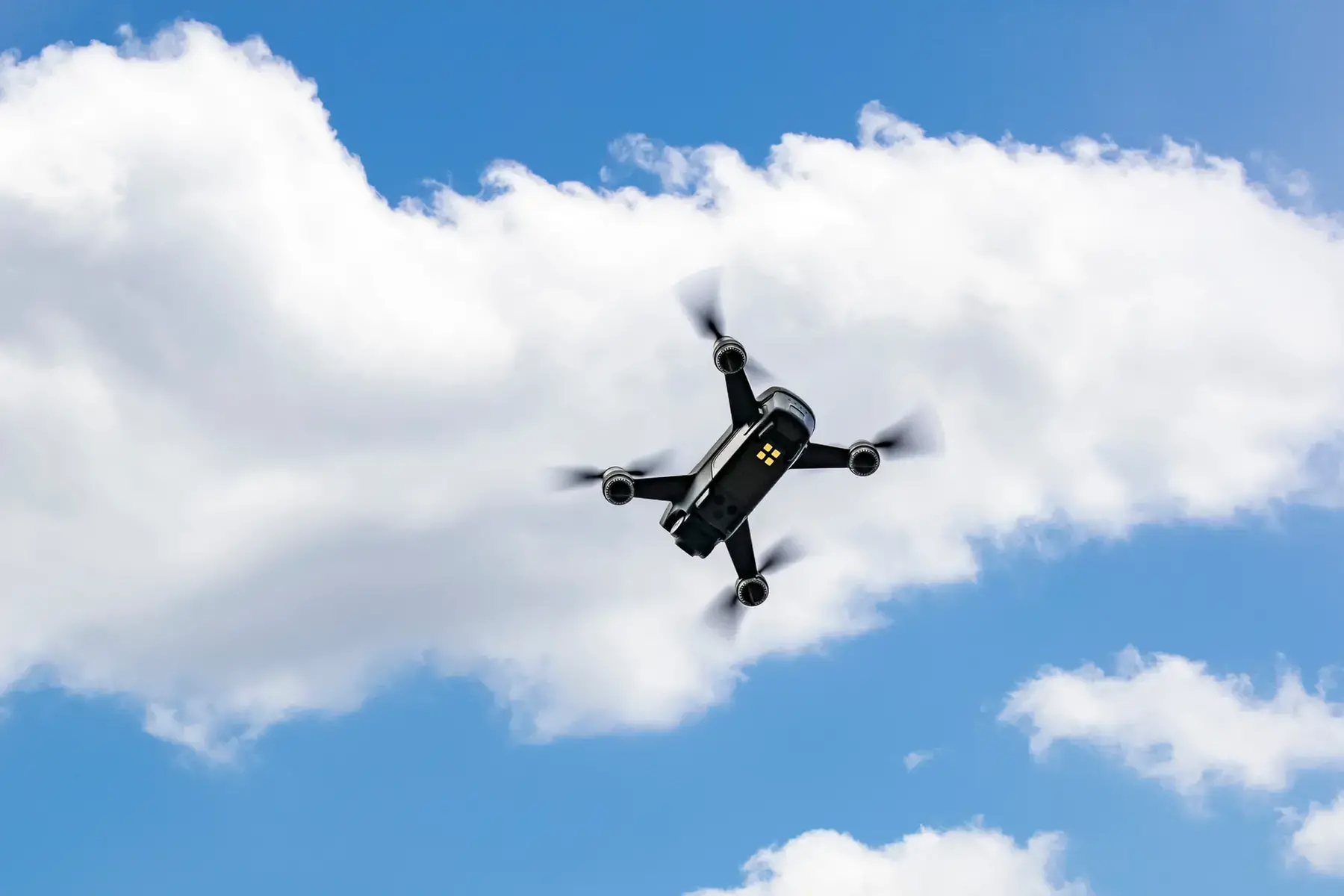 Drönare sedd underifrån där den flyger mot en blå himmel med vita moln. 