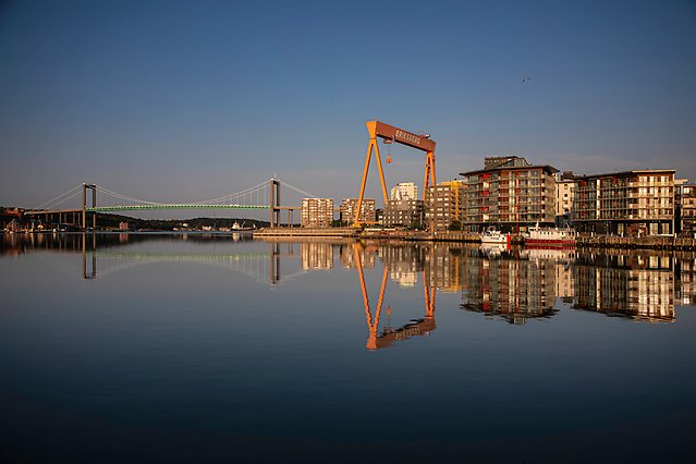 Bild på Älvsborgbron till vänster, byggnader till höger. Spegelblankt vatten framför.