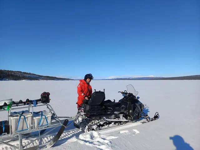 Blå himmel över istäckt sjö och man i orange overall vid scotoer