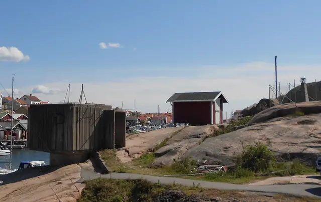 Klippa vid havet med röd stuga och båtar i bakgrund